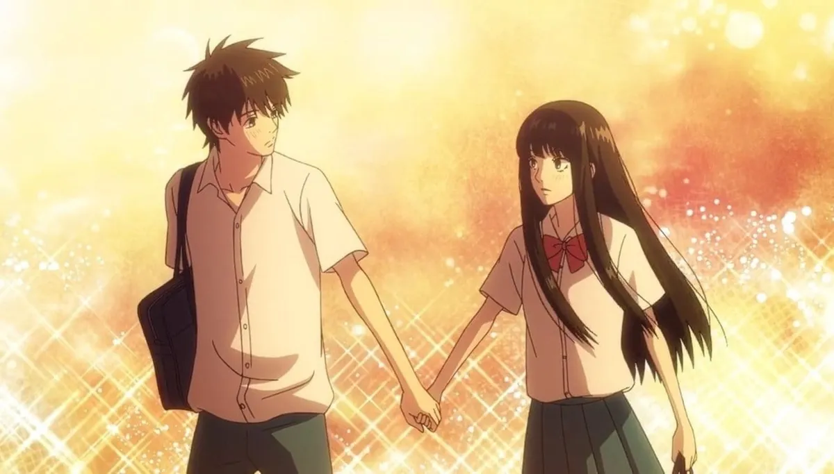 A boy in a school shirt and a girl with long black hair hold hands and look at each other in golden light, in a still from Kimi ni Todoke